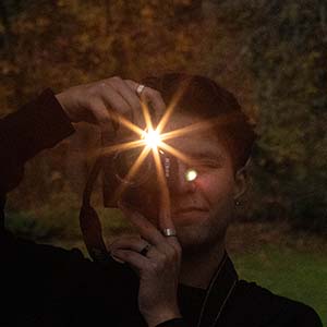 Portrait of a photographer taking a photo with a flash. The flash flare obscures his face.